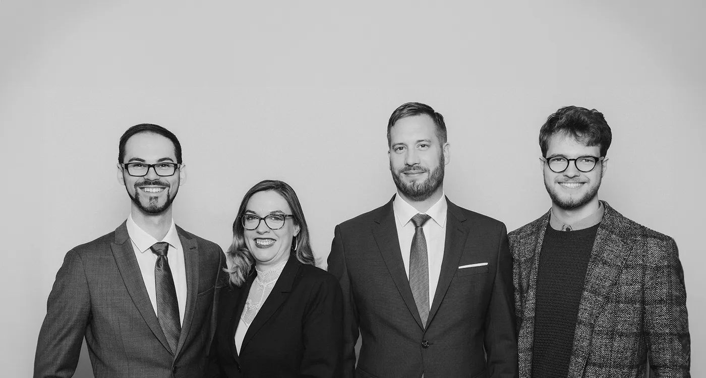 Das Team der Kanzlei Steinkugler steht nebeneinander vor einer weißen Wand.